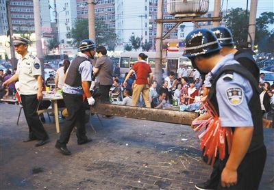 6月13日晚8點，朝陽路和青年路交叉口西側(cè)，一次聯(lián)合執(zhí)法行動中，輔警與協(xié)管抬走商戶的燒烤用具。新京報記者 尹亞飛 攝