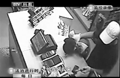 戴帽男子一手掐住加油站營(yíng)業(yè)員，一手持發(fā)令槍指向另一營(yíng)業(yè)員，要求“把錢給我裝起來(lái)”。