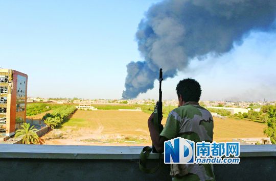 2日，利比亞首都的黎波里，一民兵武裝成員眺望被火箭彈擊中的儲(chǔ)油罐冒出濃煙。