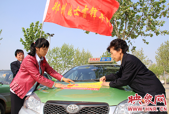 　　授旗結(jié)束后，首都的士雷鋒車隊(duì)王鳳進(jìn)隊(duì)長(zhǎng)（右）與鄭州的的哥的姐在車身上貼上標(biāo)識(shí)。