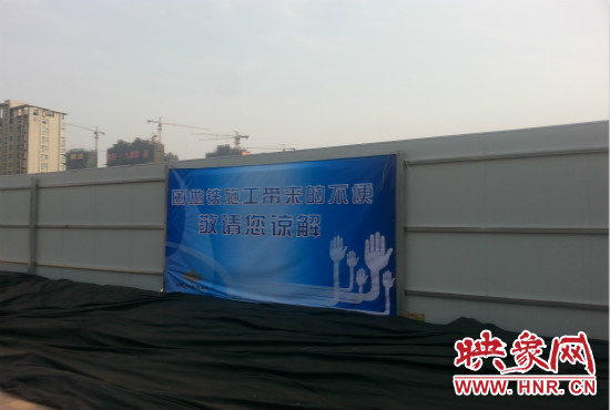 道路南側(cè)圍起了白色的圍擋，墻上標(biāo)示著“因地鐵施工帶來的不便敬請您諒解”的提示牌。