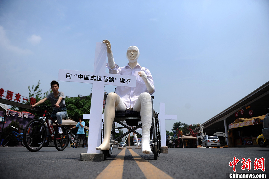 4月16日，重慶市洋人街上擺放著兩個受了傷的塑料人像“模特”，旁邊十字架上寫著向“中國式過馬路”說不