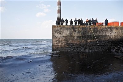 昨日，山東青島，清污人員正在海邊清理油污。