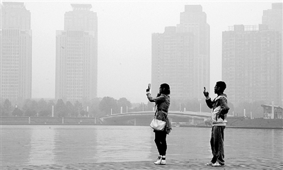 29日中午，鄭東新區(qū)如意湖畔，兩個年輕人拍攝霧霾中的景色。 鄭州晚報記者 馬健 圖