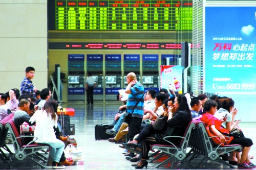 候車大廳溫度很高，一名乘客一手扇風(fēng)、一手擦汗