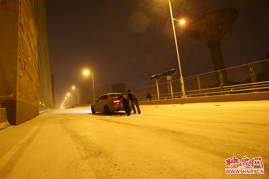 雪天路滑，汽車上橋打滑，兩名“推車人”幫助一輛私家車上坡。