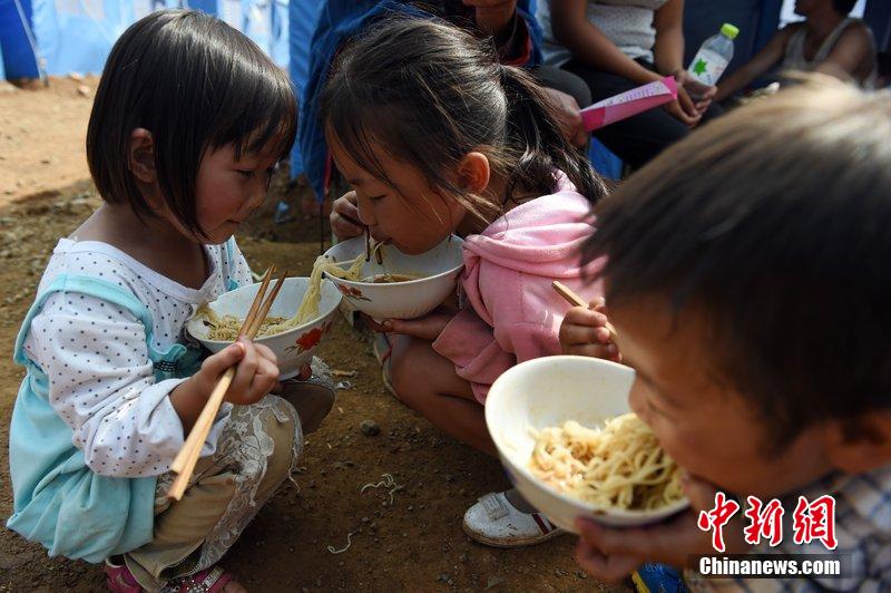 2014年8月6日，云南魯?shù)辇堫^山災(zāi)區(qū)，兒童在帳篷外吃飯。