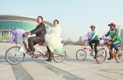 氣球和鮮花裝點(diǎn)的雙人自行車，新郎郝幸福載著美麗新娘回家。