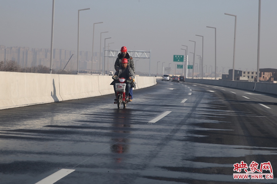 兩名工人騎車經(jīng)過(guò)灑水養(yǎng)護(hù)路面。
