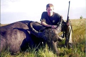 哈里王子手持獵槍，蹲在一頭遭到獵殺的水牛旁邊