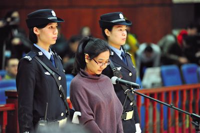 被告人盧梅低著頭，站在朝陽(yáng)法院刑事審判庭的被告席上。