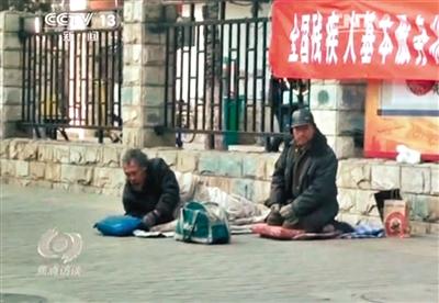 工人體育場北路，兩位乞討者路邊乞討，并輪流扮成“病人”（躺地者）。 央視截圖